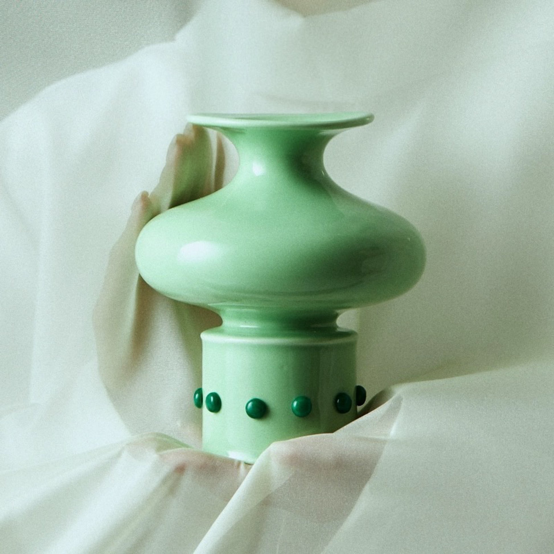 The Chinese classical bamboo-shaped green vase inlaid with green jade is gently wrapped in white gauze behind a soft hand.