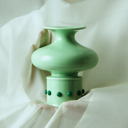The Chinese classical bamboo-shaped green vase inlaid with green jade is gently wrapped in white gauze behind a soft hand.