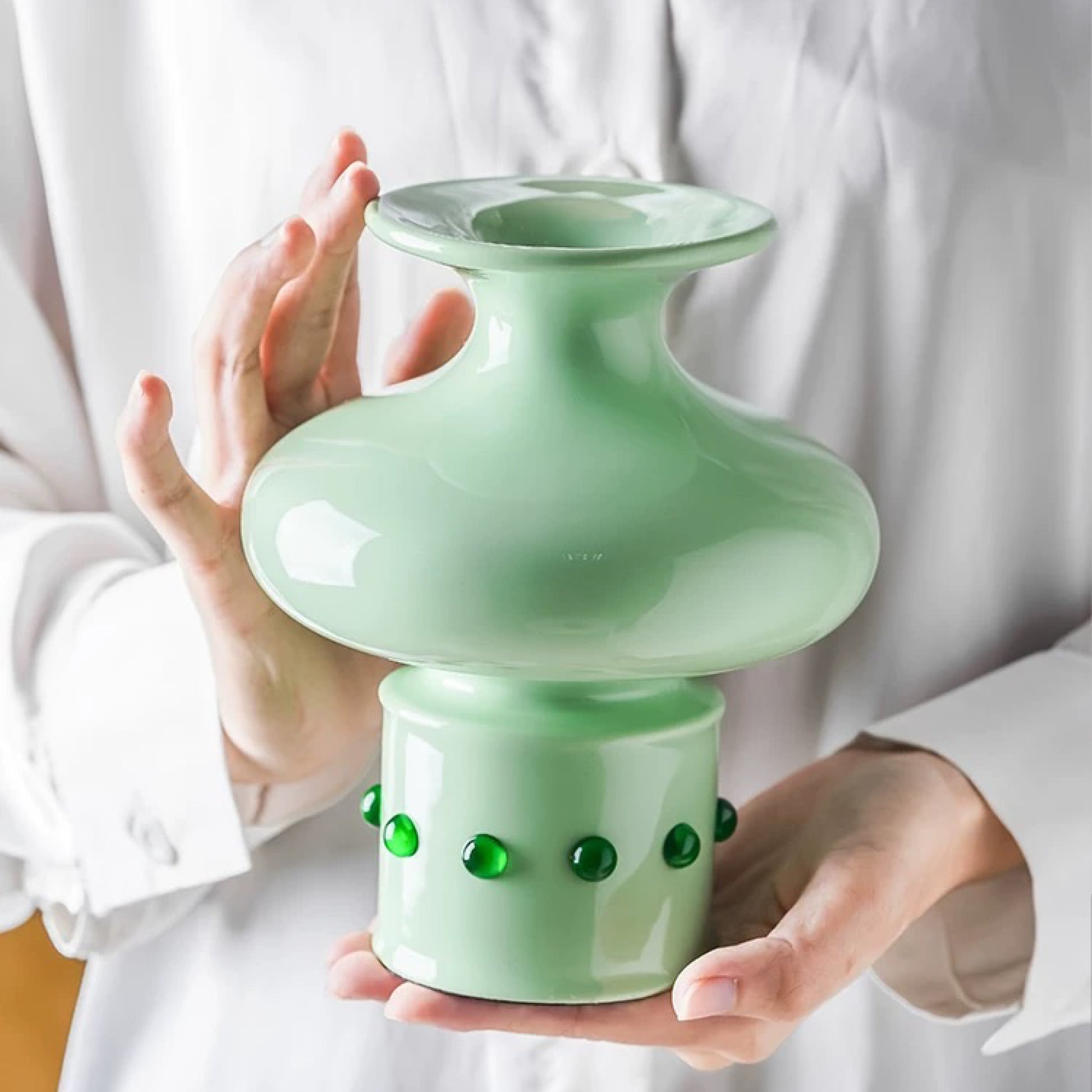 A hand holding a jade green vase with a classic Chinese bamboo joint design, inlaid with green jade at the base.