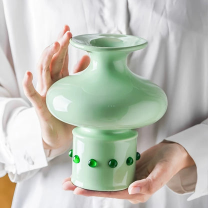 A hand holding a jade green vase with a classic Chinese bamboo joint design, inlaid with green jade at the base.